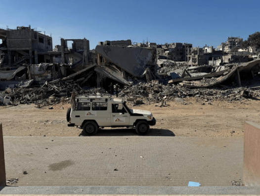 An MSF vehicle is parked outside Al Rantisi Hospital in Gaza City, amidst the rubble and destruction in the area. The photo, taken from the hospital’s entrance, looks out onto the street.